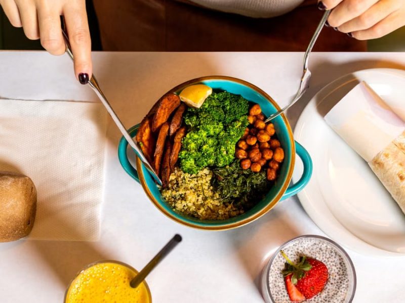 A vibrant vegan meal with fresh ingredients like broccoli, chickpeas, quinoa, served alongside a burrito and refreshing drinks.
