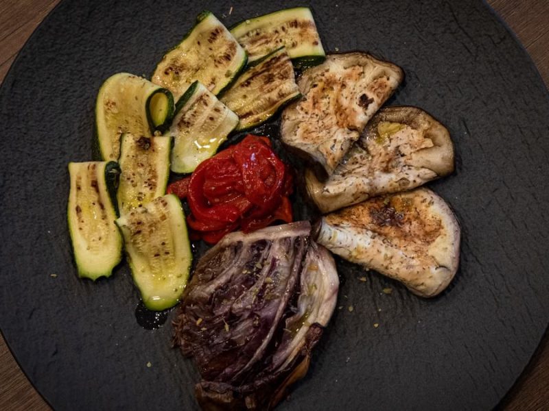 A delectable assortment of grilled vegetables on a rustic black plate, accented with olive oil and spices.